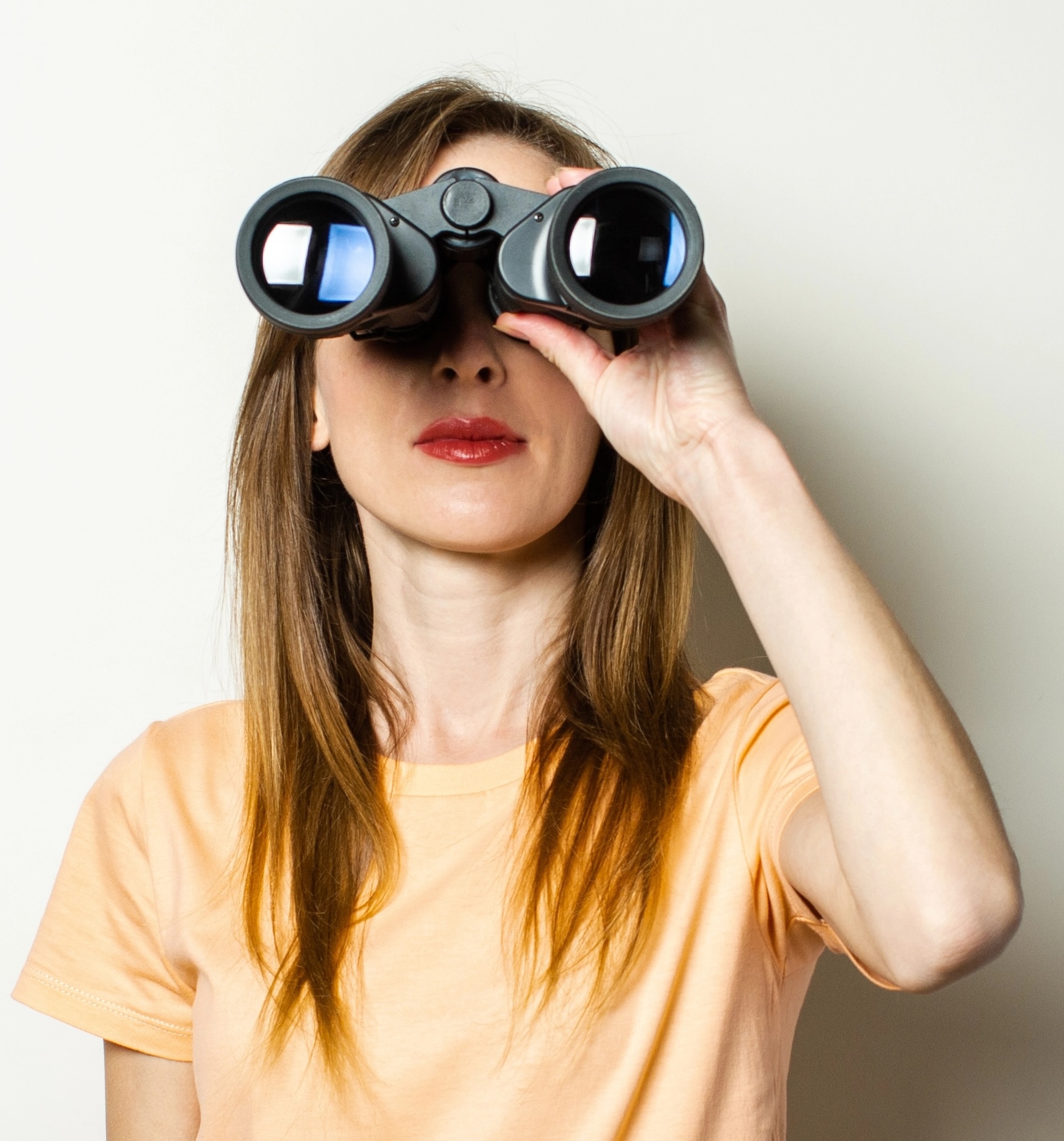 Young friendly girl looking through binoculars on a light background. Banner. Emotional face.